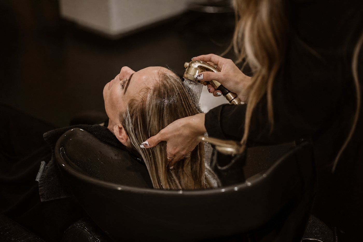 A client receiving a shampoo service at a black bowl with gold fixtures at Von Rae
